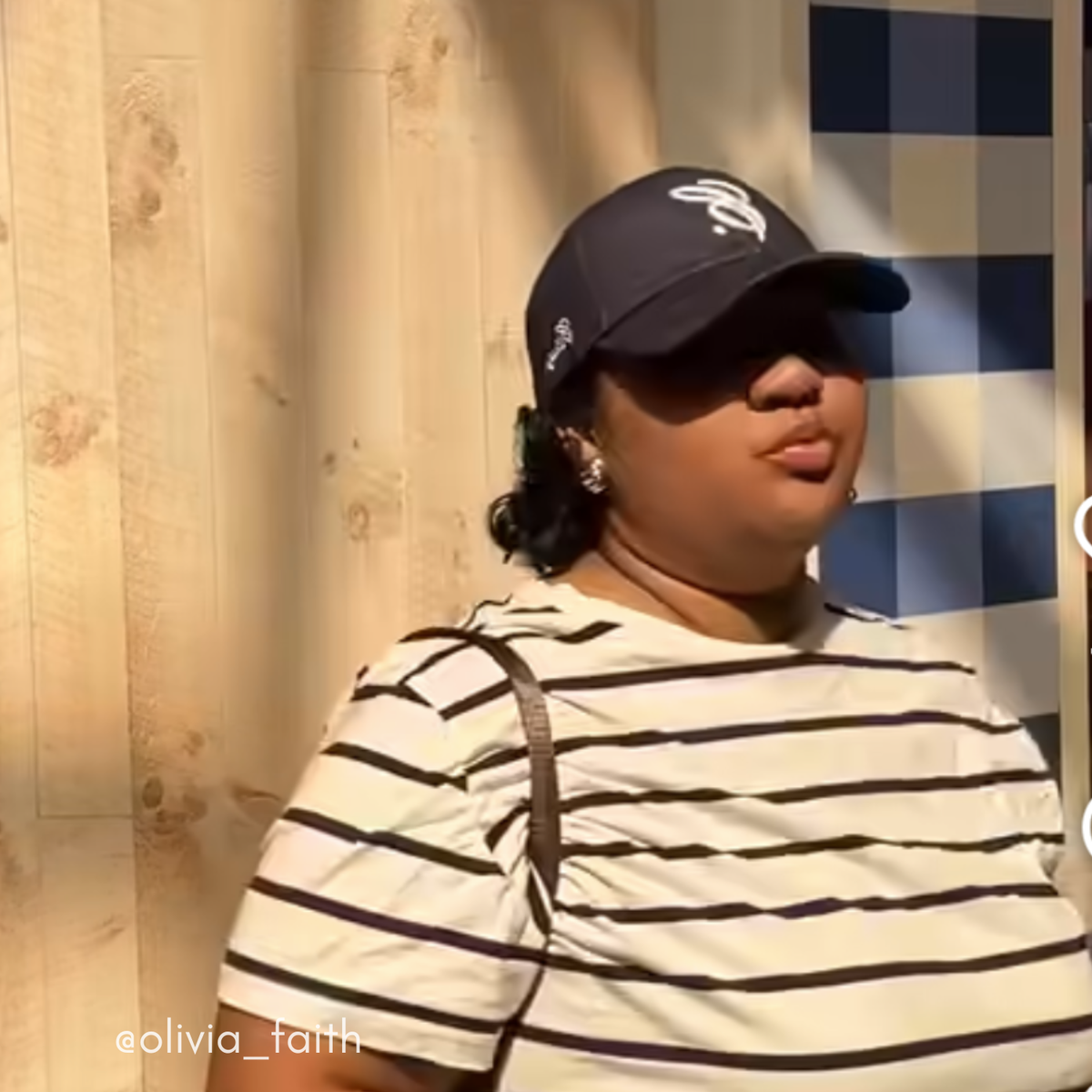 Person wearing a striped shirt and cap against a checkered curtain background