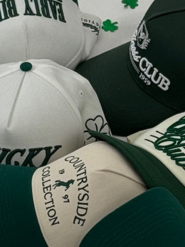 Collection of baseball caps with various logos on a white background with green shamrock patterns.
