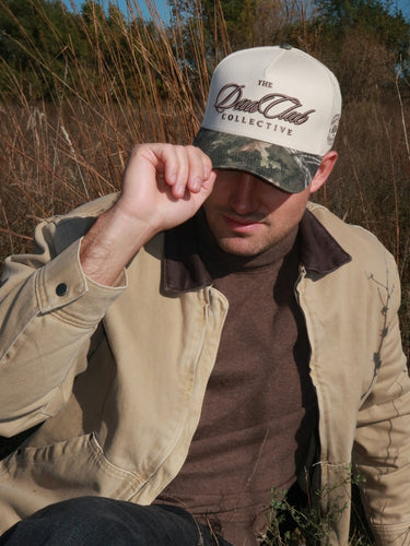 Man wearing a camo 'The Dad Club Collective' logo in a natural setting
